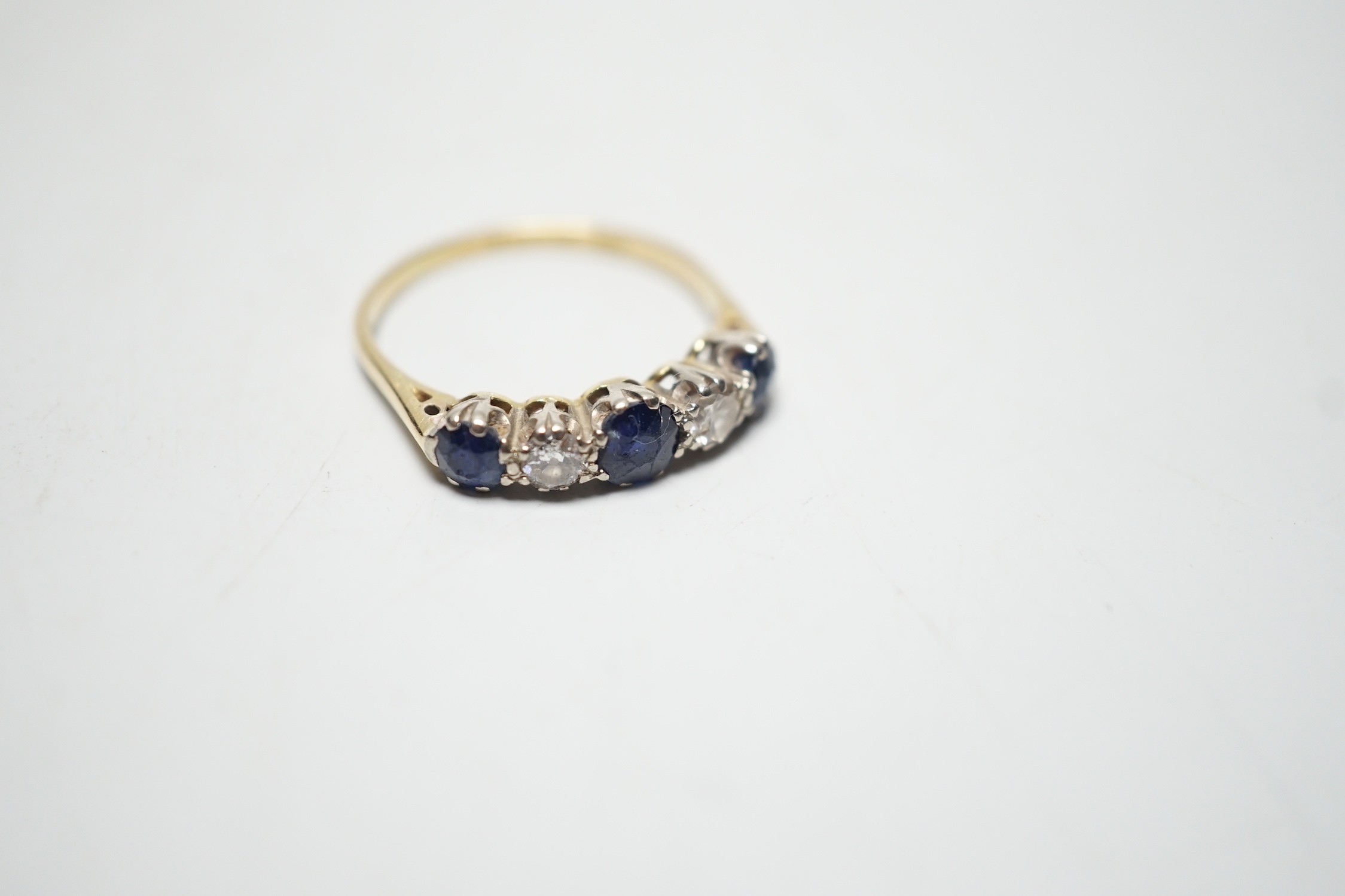 A modern 18ct gold, three stone sapphire and two stone diamond set half hoop ring, size R, gross weight 3.1 grams.